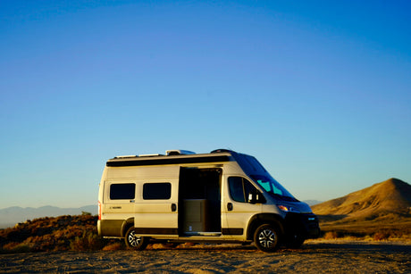 Modern campervan, ideal for RV rental, parked in a vast desert landscape with its side door open under a clear sky.