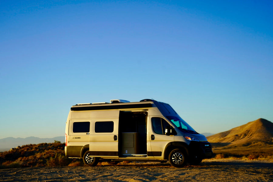 Modern campervan, ideal for RV rental, parked in a vast desert landscape with its side door open under a clear sky.