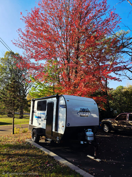 A white Clipper RV rental travel trailer is parked under a brilliant red maple tree, showcasing a vibrant autumn camping scene.
