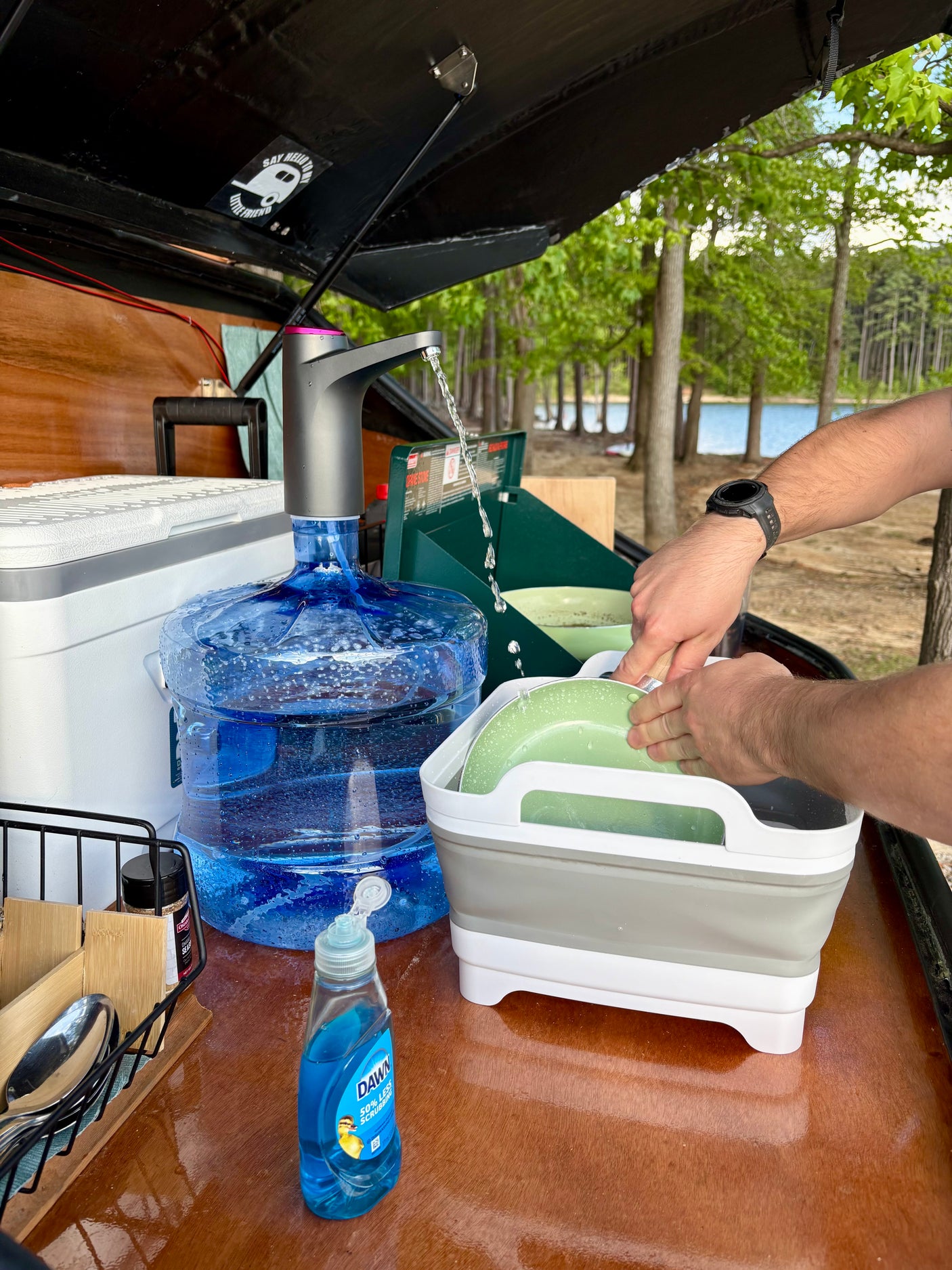 RV rental outdoor kitchen setup: Washing dishes at a scenic campsite by the lake. Portable water & collapsible sink.