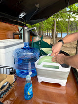 RV rental outdoor kitchen setup: Washing dishes at a scenic campsite by the lake. Portable water & collapsible sink.