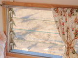 Louvered window with a cowboy-patterned curtain inside an RV rental, offering a view of the outdoors.