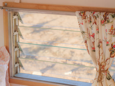 Louvered window with a cowboy-patterned curtain inside an RV rental, offering a view of the outdoors.