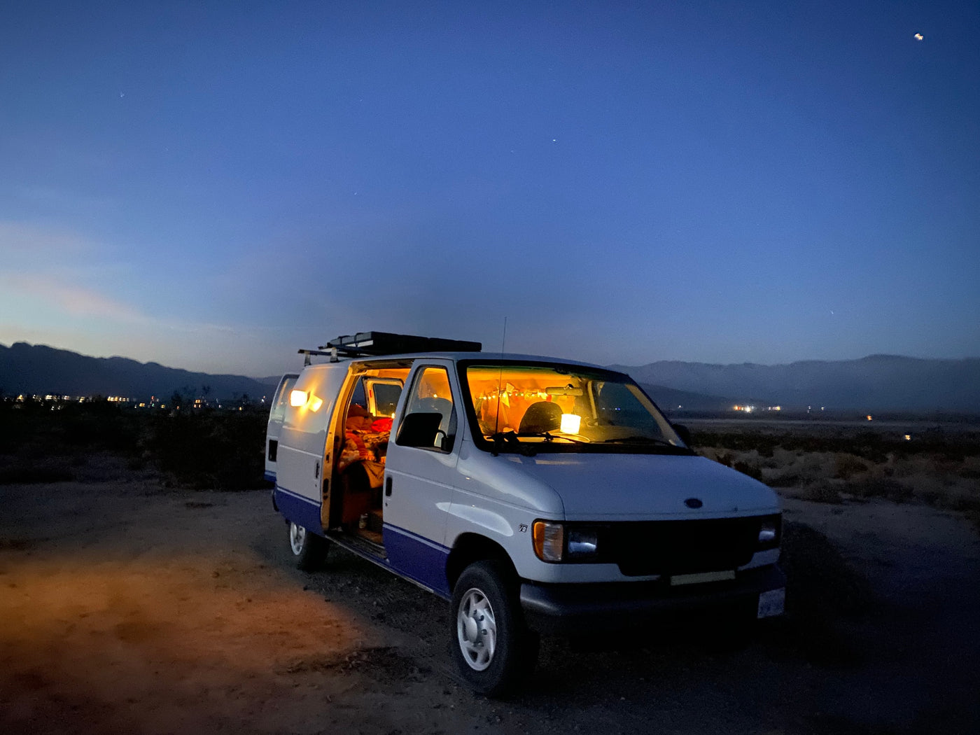 A welcoming rv rental, glowing warmly inside, parked in a vast desert landscape under a dark blue, starry sky at dusk. — photo 12