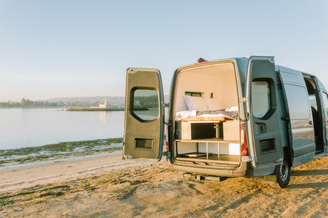 Scenic RV rental parked on a sandy beach at golden hour, revealing its comfortable bed and storage in the back.