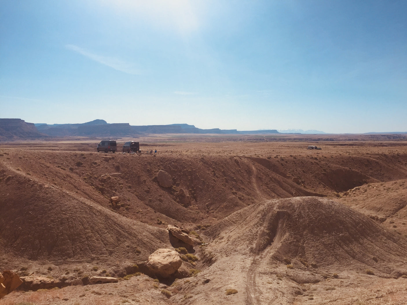 Vast desert landscape with multiple RV rental vans parked among red hills, ideal for off-grid camping adventures.