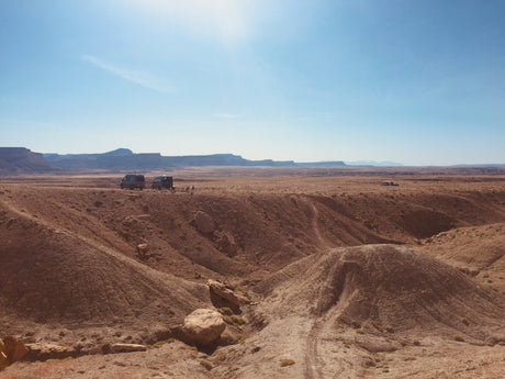 Vast desert landscape with multiple RV rental vans parked among red hills, ideal for off-grid camping adventures.
