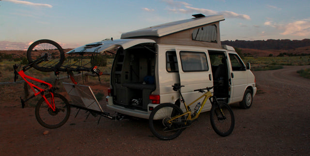 White pop-top camper van (RV rental) with two mountain bikes ready for adventure. Parked on a dirt road at dusk.