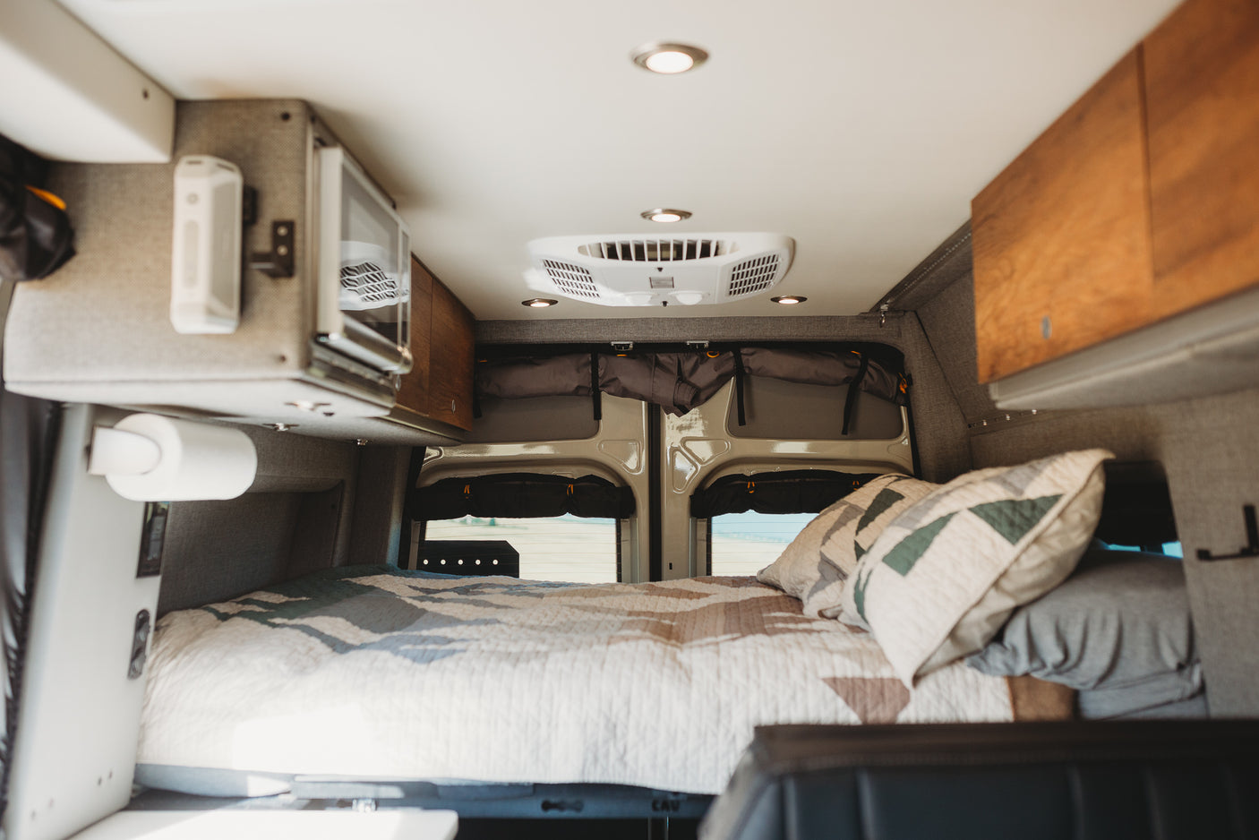 Interior of an RV rental camper van, featuring a cozy bed, microwave, and ceiling AC. Perfect for travel.