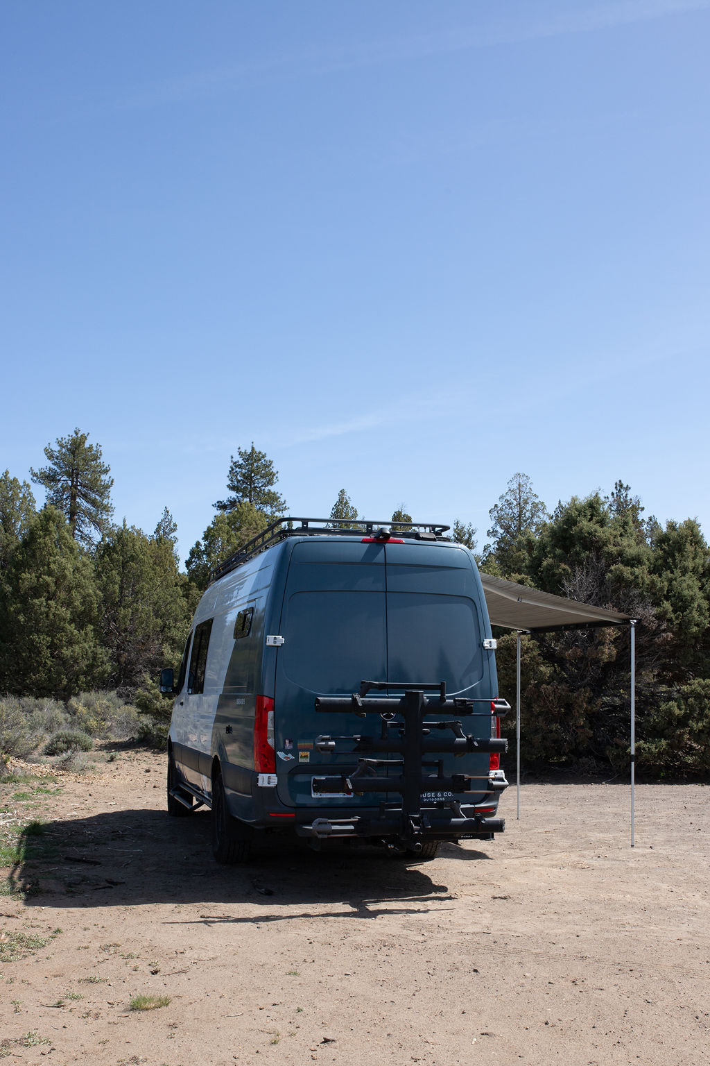  snow-capped mountains in background. Awning extended.|White and teal camper van RV rental with awning extended