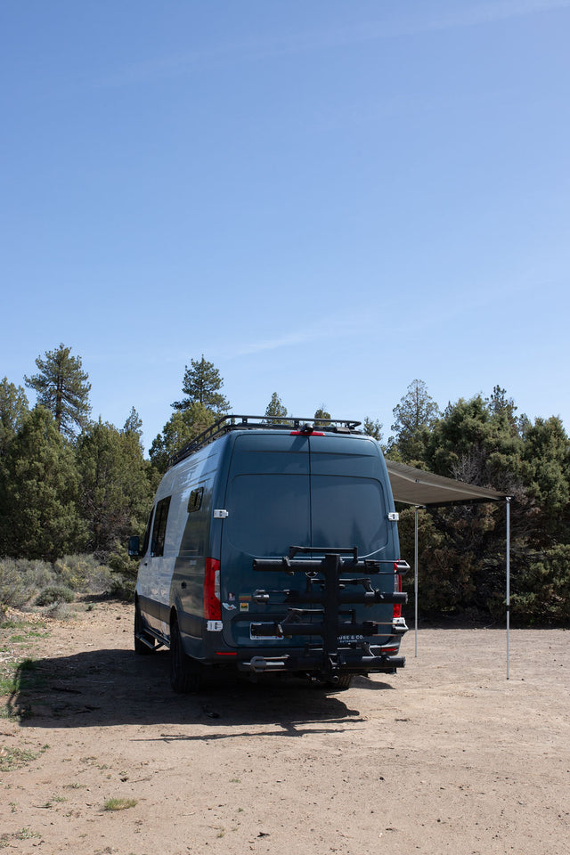  snow-capped mountains in background. Awning extended.|White and teal camper van RV rental with awning extended