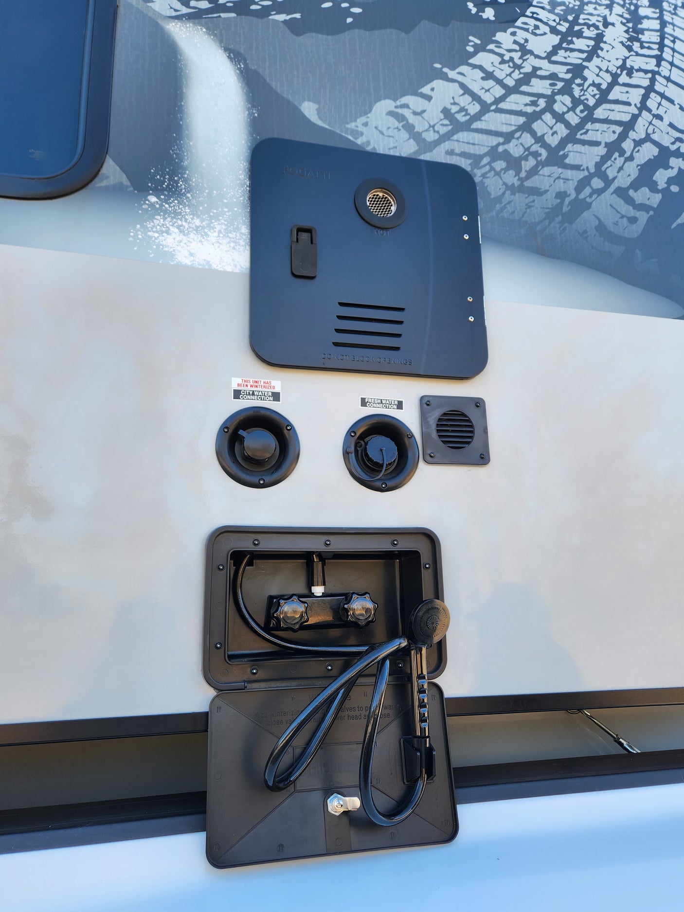 This RV rental's exterior utility panel features a water heater, city and fresh water connections, and a convenient outdoor shower.