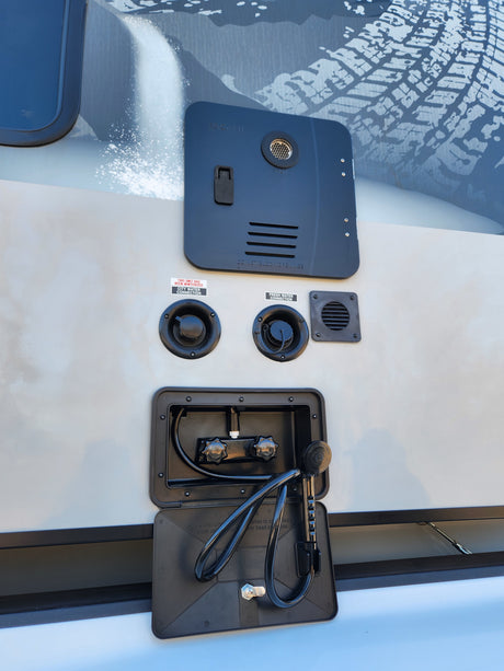 This RV rental's exterior utility panel features a water heater, city and fresh water connections, and a convenient outdoor shower.