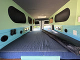 Inside a modern RV rental: view of custom interior with twin beds, built-in storage, and unique color scheme.