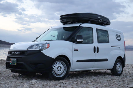 A white Ram ProMaster City van with a roof cargo box on a rocky shore. Perfect for your next RV rental adventure.
