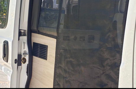 RV rental camper van interior. Black bug screen door with light wood paneling and a black ventilation vent by the door entrance.