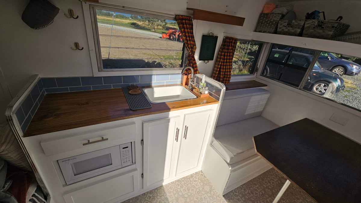 Cozy RV rental interior: kitchenette with wood counters, blue tiles, microwave. Dining nook & storage baskets. — photo 6