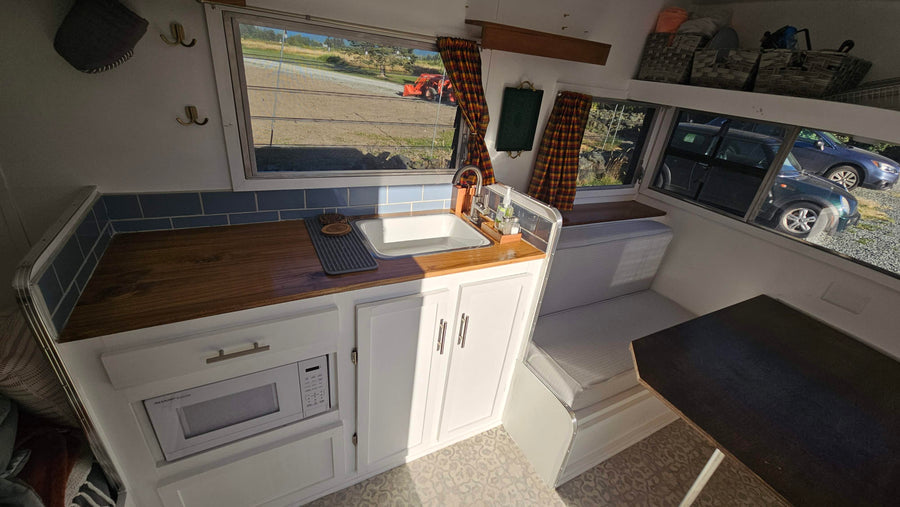 Cozy RV rental interior: kitchenette with wood counters, blue tiles, microwave. Dining nook & storage baskets.