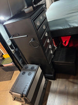 Compact RV rental: black dresser, cozy bed, & portable cooler. Maximize space for travel.