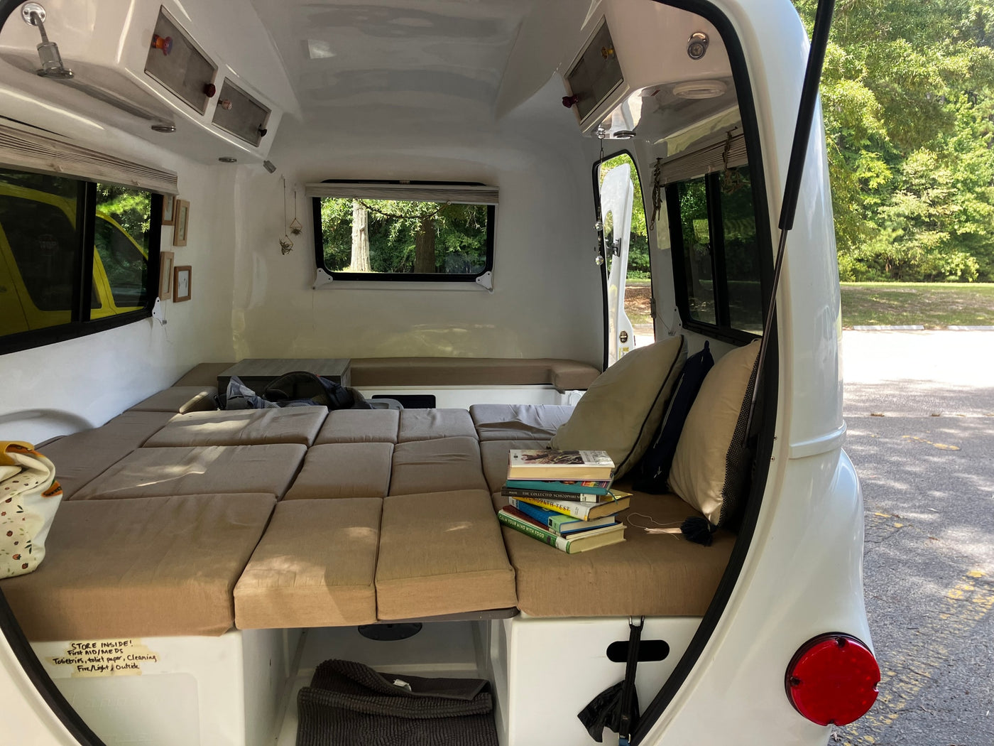 Inside a compact RV rental: a plush bed, stack of books, and smart storage solutions for travelers. — photo 4