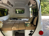 Inside a compact RV rental: a plush bed, stack of books, and smart storage solutions for travelers.