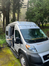Discover adventure: a silver RV rental camper van parked amidst misty trees, with its side door open revealing the interior.