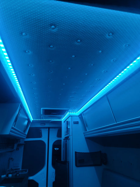 Inside an RV rental, glowing blue LED strip lights illuminate the textured ceiling and built-in storage cabinets.