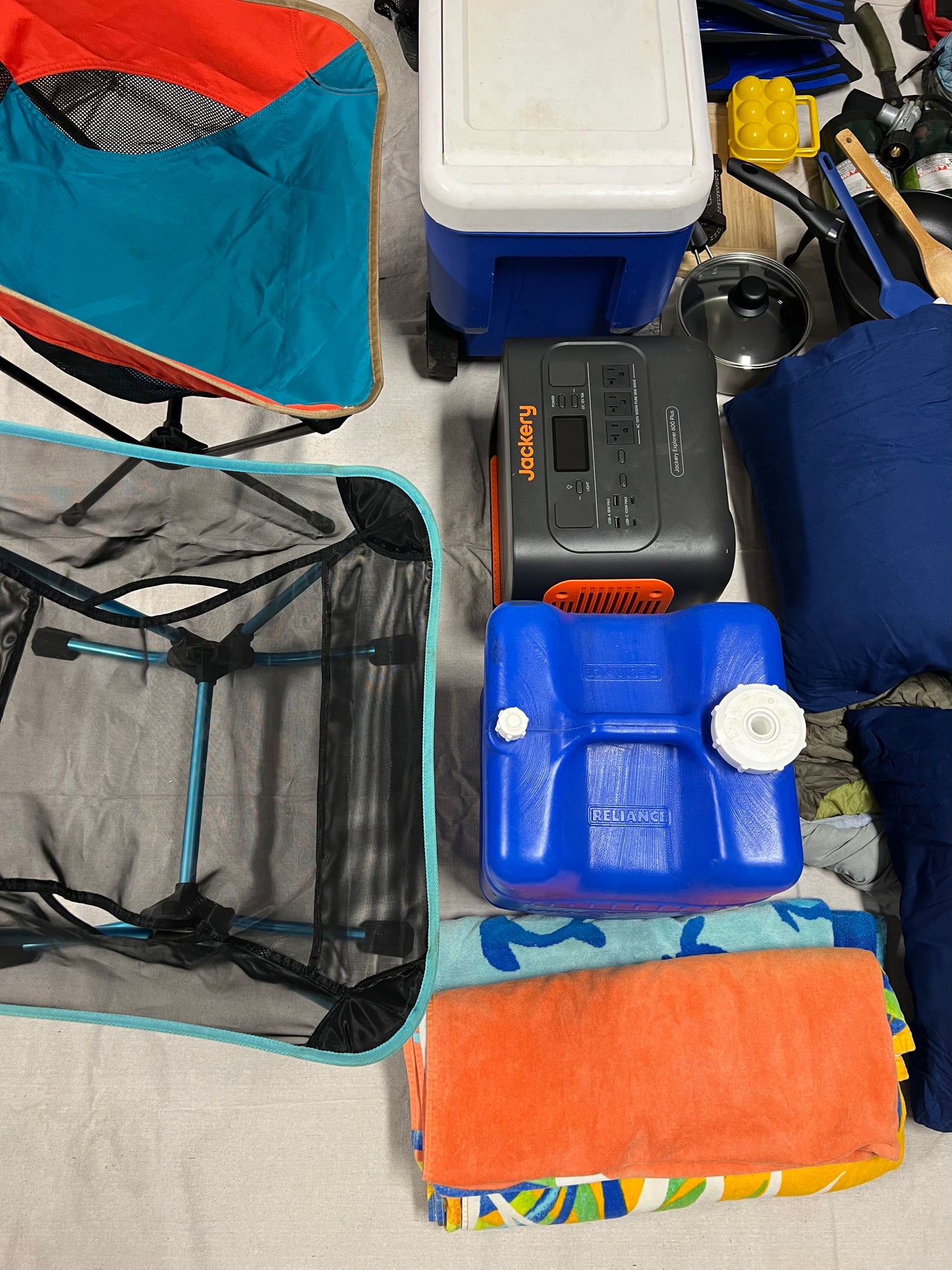 Preparing for an RV rental trip with essential camping gear: portable power station, cooler, water container, chairs, & kitchen items.