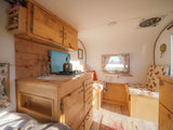 Rustic RV rental interior with wooden kitchen, bed, and dining nook. Compact and cozy space.