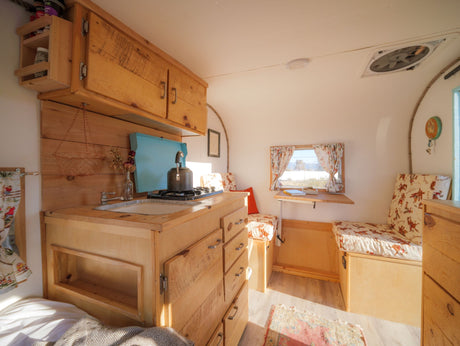 Rustic RV rental interior with wooden kitchen, bed, and dining nook. Compact and cozy space.