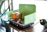 Cooking on a portable green Coleman propane stove with a copper pot, set up in an RV rental for easy camper van meals.