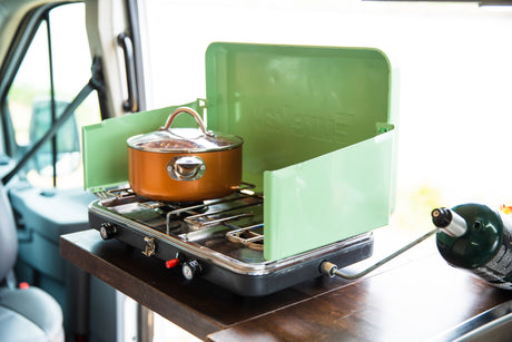 Cooking on a portable green Coleman propane stove with a copper pot, set up in an RV rental for easy camper van meals.
