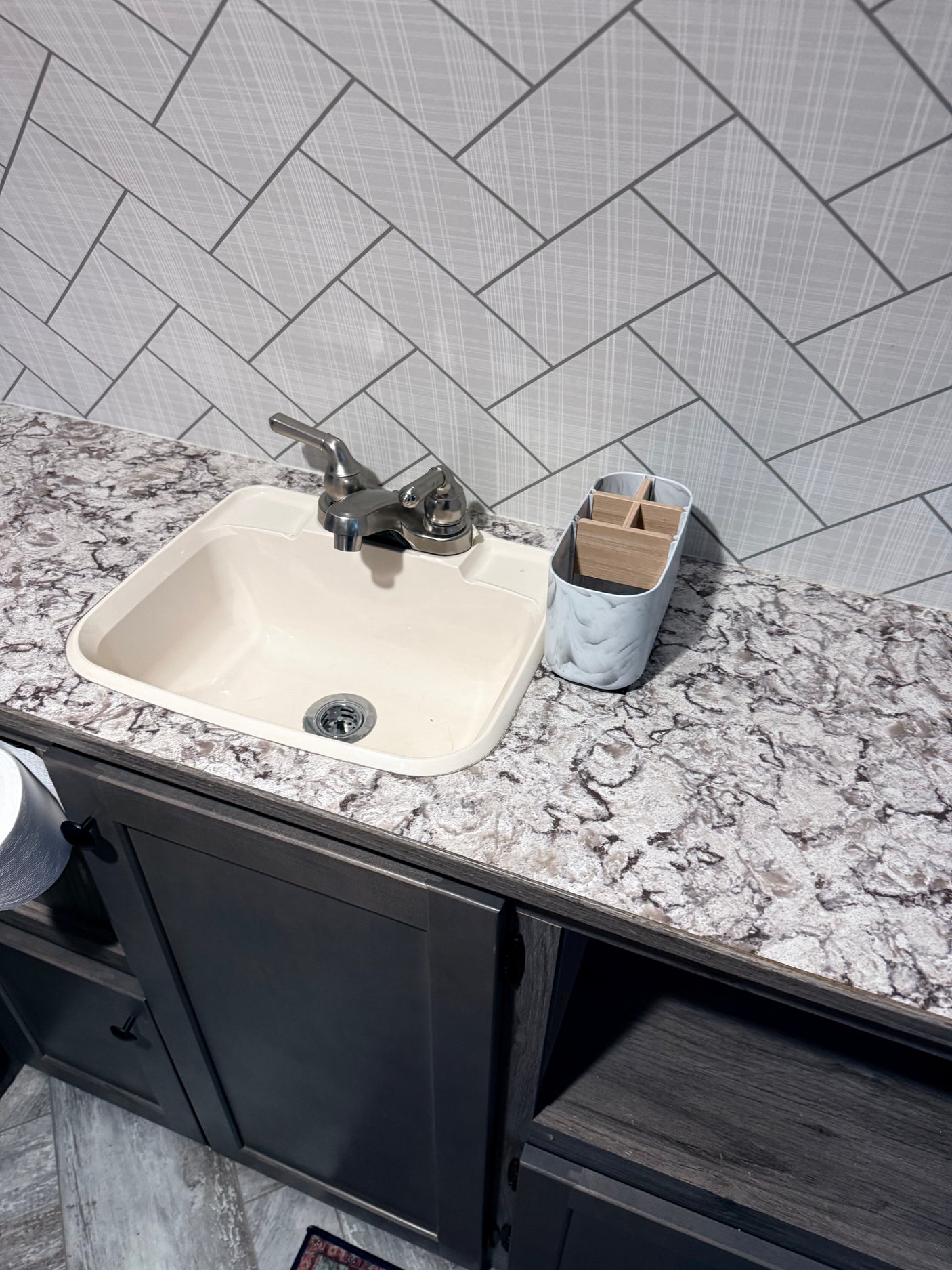 Functional RV rental kitchen/bathroom with a cream sink, mottled gray countertop, herringbone backsplash, and dark cabinets.