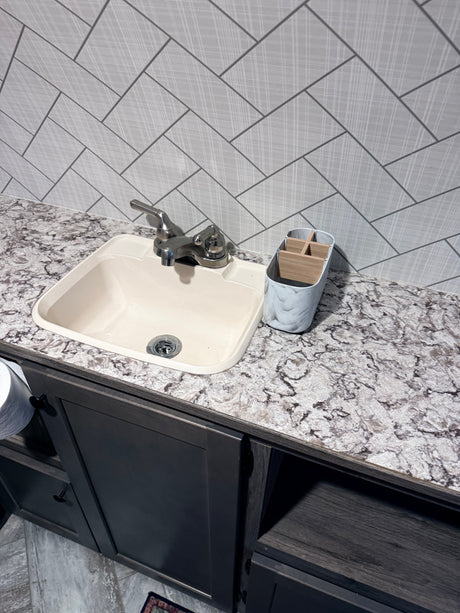 Functional RV rental kitchen/bathroom with a cream sink, mottled gray countertop, herringbone backsplash, and dark cabinets.