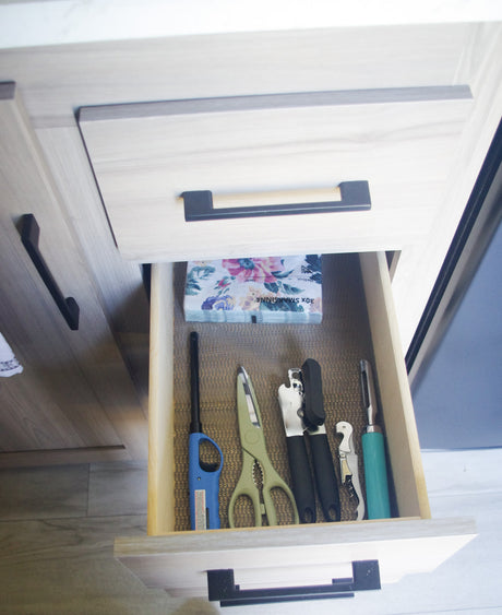 Open kitchen drawer in an RV rental, neatly stocked with camping kitchen essentials: a lighter, can opener, and floral napkins.
