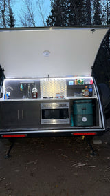 RV rental: Modern camper galley with sink, microwave, stove, & cooler for outdoor cooking adventures.