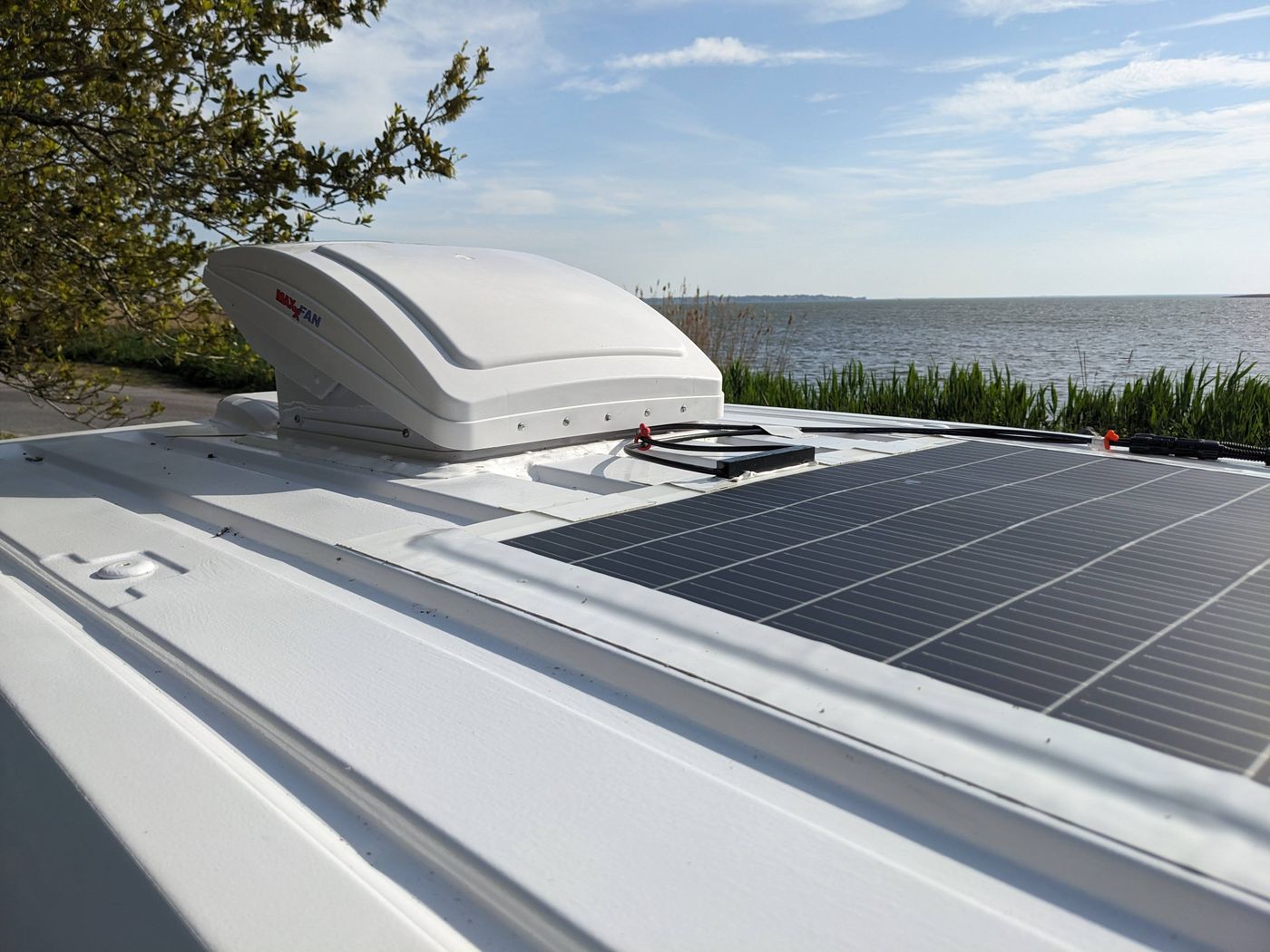 RV rental: rooftop solar panels, vent fan, and a serene water view from the van.
