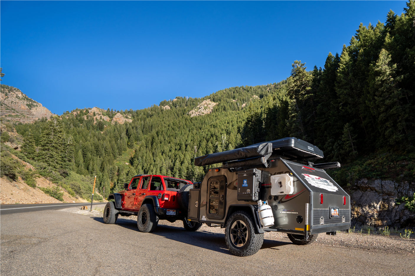 Red Jeep + rugged overland camper parked roadside in mountains, clear sky. Perfect for your next RV rental adventure!