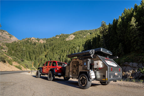 Red Jeep + rugged overland camper parked roadside in mountains, clear sky. Perfect for your next RV rental adventure!
