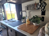 Cozy rv rental kitchen with sink, plants, and cutting board, showcasing a compact yet functional interior.