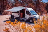 White RV rental with extended awning and camping chairs, ready for outdoor living, parked in an arid landscape.