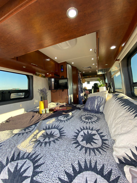 This RV rental's inviting interior offers a comfortable bed with a unique quilt, TV, and warm lighting.