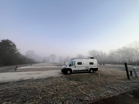 Serene foggy, frosty morning at a quiet RV park. White camper van (RV rental) parked on frosted grass.