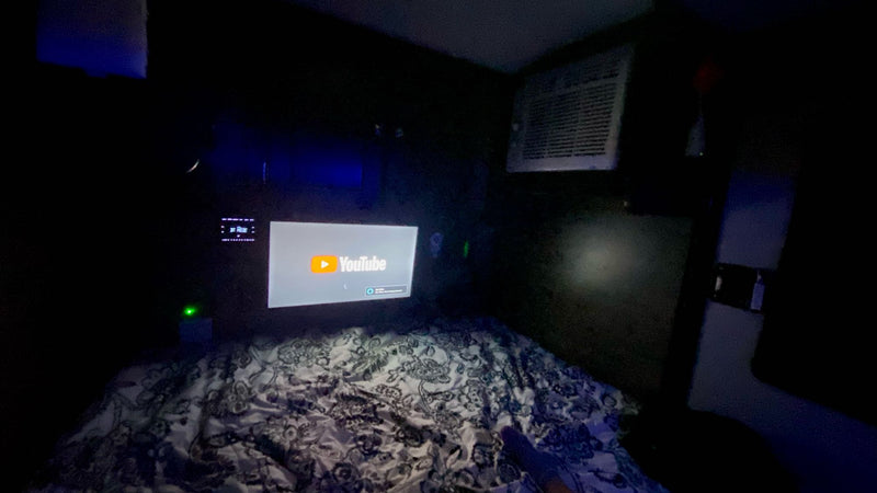 Cozy RV rental interior: YouTube projected on the wall above a patterned bed, with an AC unit visible. — photo 12