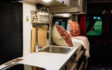 Inside a cozy RV rental: compact kitchen with sink, comfy seating, and a window revealing a green view.
