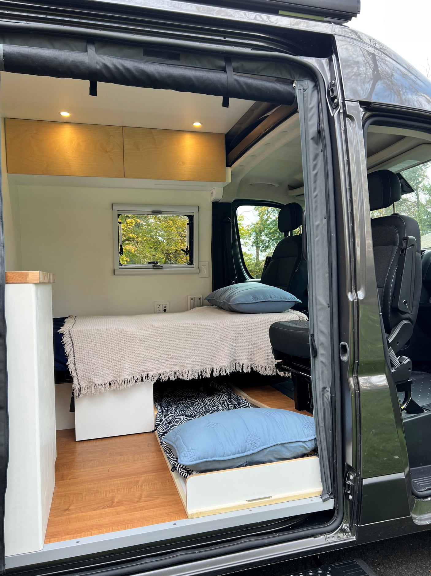 Spacious RV rental interior with bed, pull-out storage, wood cabinets, and front seats. View from open door.