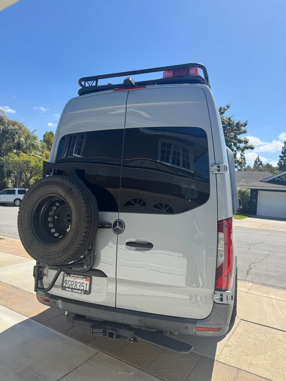 Rear view of a light grey Mercedes-Benz Sprinter camper van, fitted with a roof rack & spare tire, ideal for rv rental adventures. — photo 20