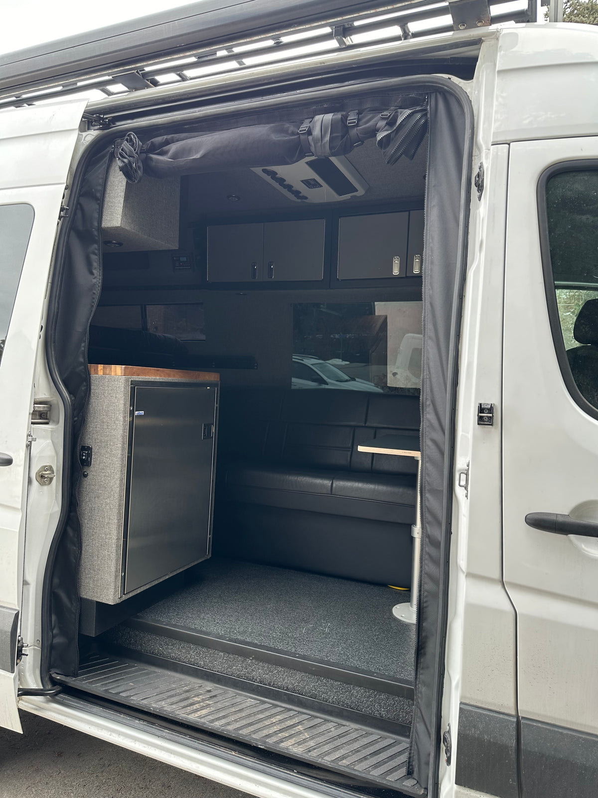 View of an RV rental camper van interior through an open side door, showcasing a kitchen, fridge, and seating area. — photo 2