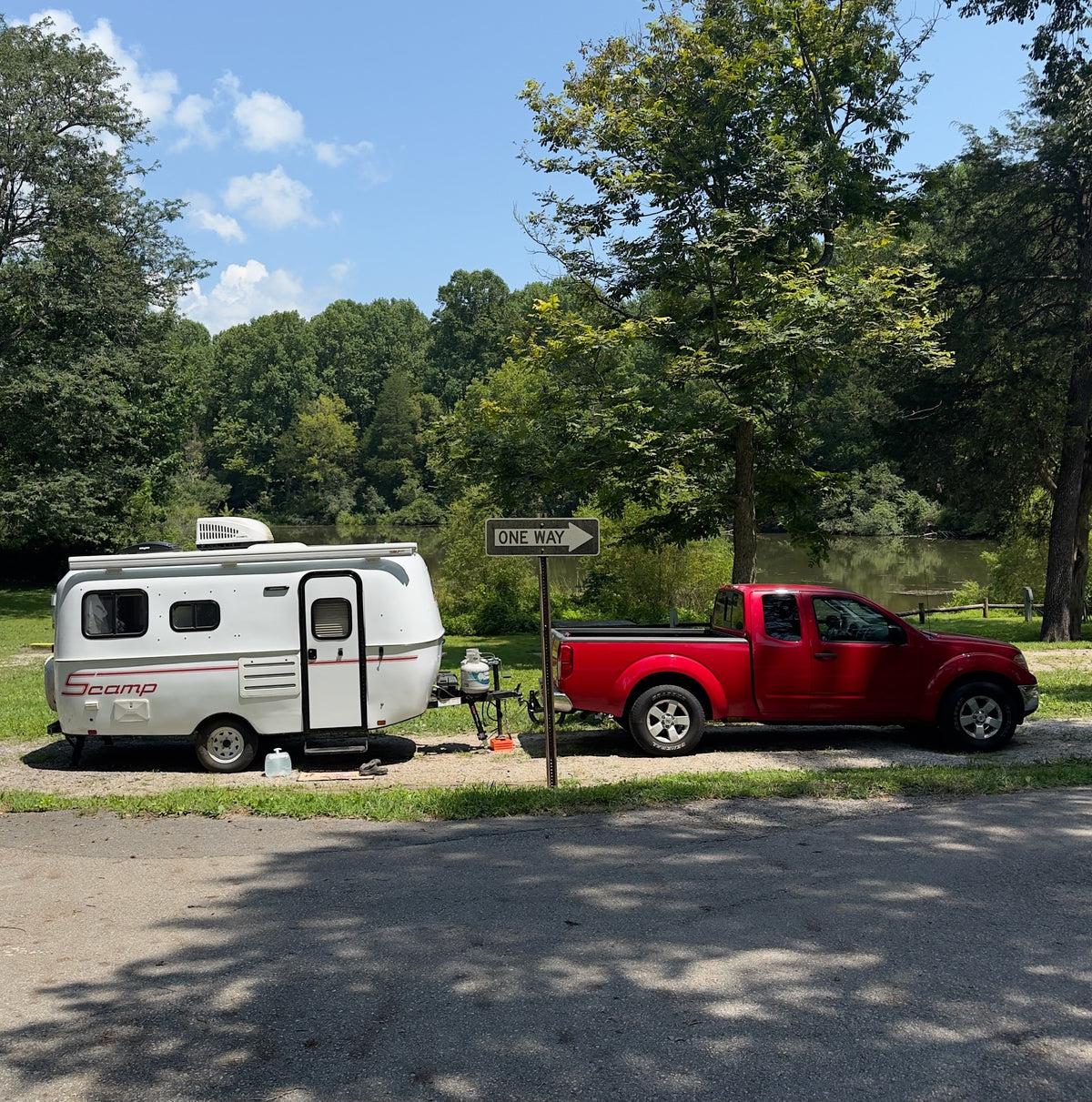 An rv rental, a white Scamp trailer towed by a red pickup truck, parked beside a lake surrounded by trees. — photo 3