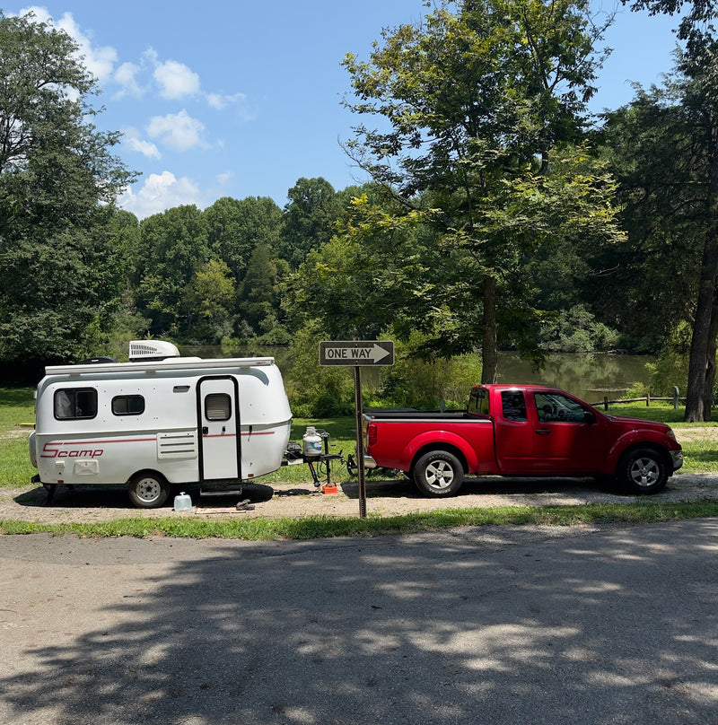 An rv rental, a white Scamp trailer towed by a red pickup truck, parked beside a lake surrounded by trees. — photo 3